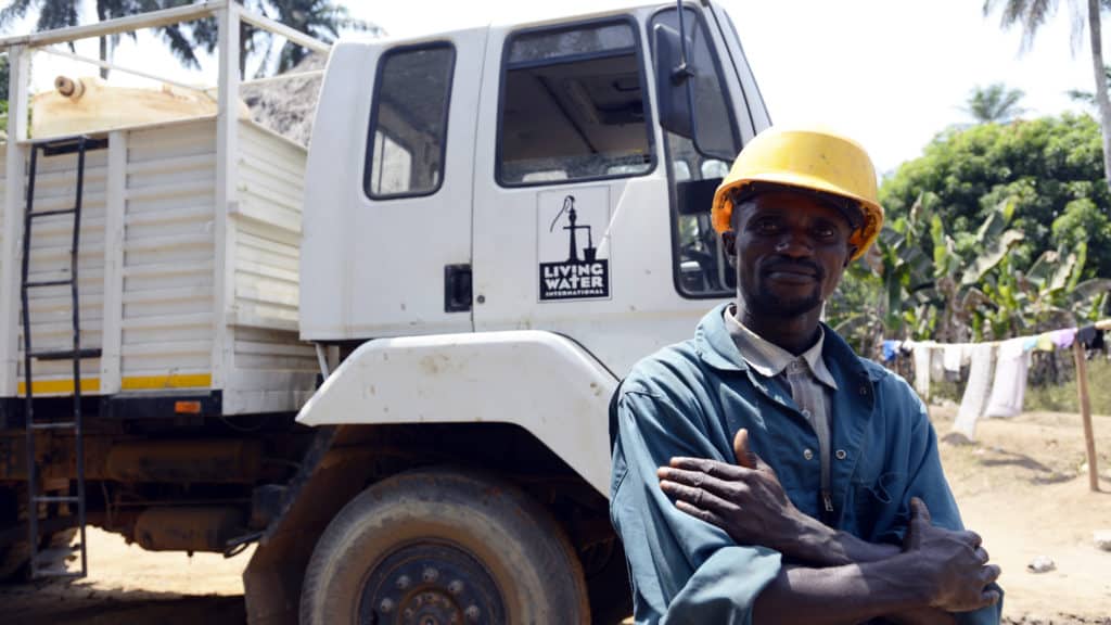 A Living Water driller in Sierra Leone stands in front of drilling rig.